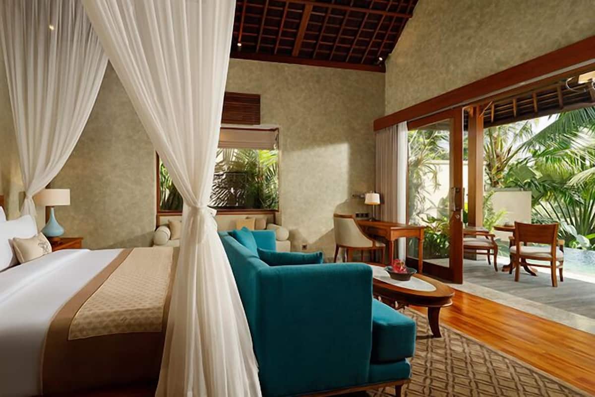 A spacious bedroom with a large bed, a sitting area with a sofa and chairs, and a balcony with a view of greenery.