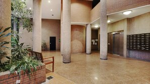 Un hall d’entrée spacieux avec de hauts plafonds, de grandes colonnes, un jardin en briques agrémenté de plantes et un ascenseur.