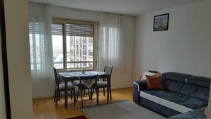 Un salon avec un canapé, une table à manger et des chaises, et une vue par la fenêtre.