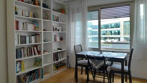 Une pièce comprenant une grande bibliothèque remplie de livres, une table à manger avec des chaises et une fenêtre avec des stores.