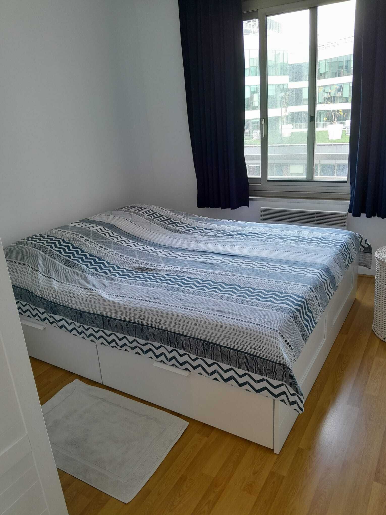 Un dormitorio con cama, ventana y vista a edificios.