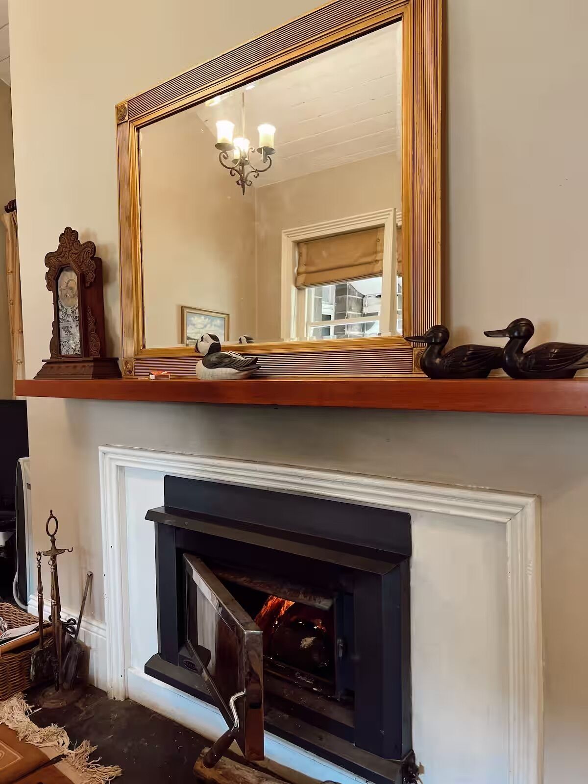 A room with a large mirror above a fireplace, a chandelier, and decorative items including a clock and swans.