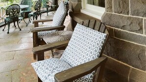 A covered patio area with stone walls, wooden furniture, and green metal chairs.
