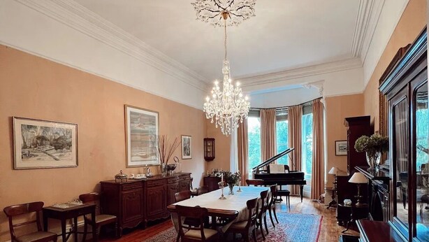 A spacious living room with a dining area, a grand piano, and a chandelier.