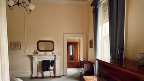 A bedroom with a bed, dresser, vanity, and a mirror. There is a hallway leading to another room.