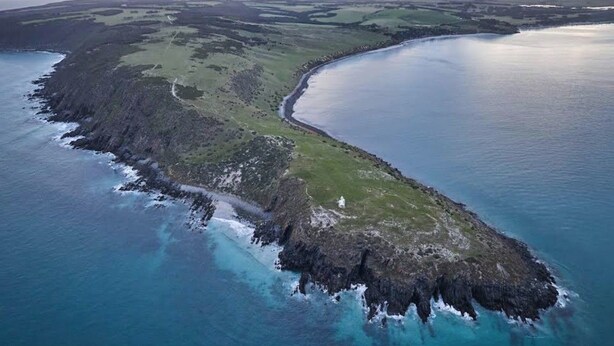 An aerial view of a coastal landscape with a narrow strip of land leading to a body of water, surrounded by green fields and rocky terrain. - Cabn Kangaroo Island (Ironstone)