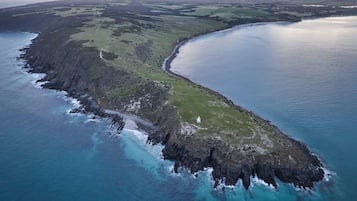 An aerial view of a coastal landscape with a narrow strip of land leading to a body of water, surrounded by green fields and rocky terrain.