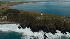 A coastal landscape with a lighthouse, rocky cliffs, and a body of water. - Cabn Kangaroo Island (Ironstone)