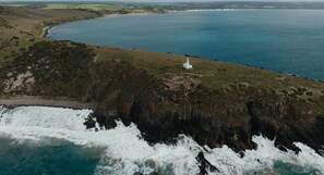 Paesaggio costiero con un faro, scogliere rocciose e un tratto d'acqua.