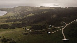 Vista aérea de una zona costera con una carretera serpenteante y varios edificios.