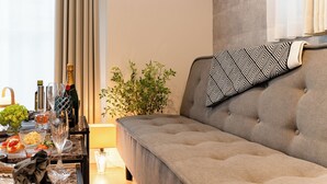Een moderne woonkamer met een grijze bank, een gekleurd kussen, een kleine plant en een eethoek met een tafel gedekt voor een maaltijd.