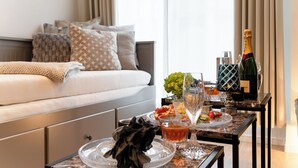 Een moderne hotelkamer met een bed, een eettafel met glazen blad en een fles champagne.