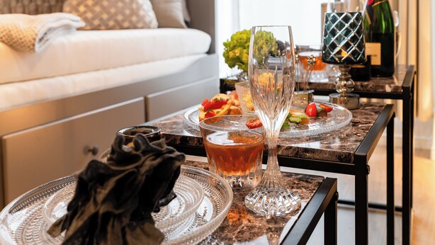 Een eettafel met een glas amberkleurig vocht, een decoratief glas en een fles champagne.