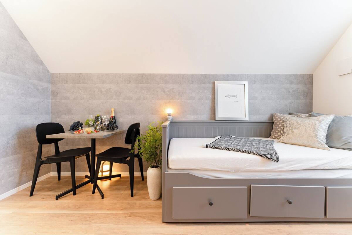 Una camera compatta con un letto, comodini, una scrivania con sedie e una piccola pianta in vaso.