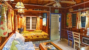 A cozy room with a bed, sofa, and a coffee table. There is a ceiling fan, a window with curtains, and a door. - Fare Miti (Moorea-Maiao)