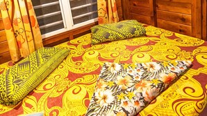 A wooden cabin room with a bed, curtains, a window, and a beach painting. - Fare Miti (Moorea-Maiao)