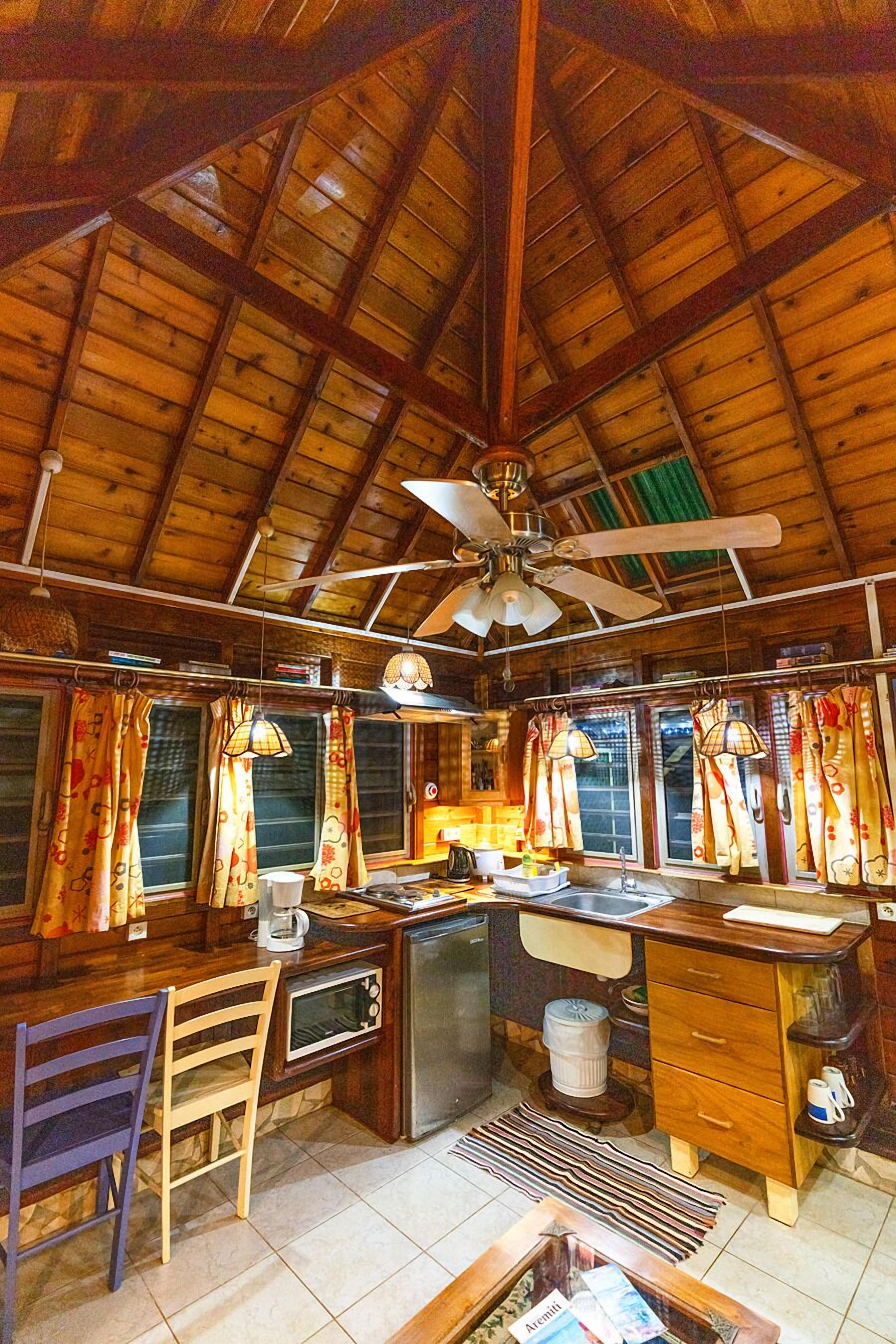 Una cocina rústica con vigas de madera, ventilador de techo y una barra con una silla y mostrador.