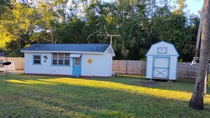 A small white house with a blue door and windows, a shed with a blue door, and a fenced yard. - Charming 1-bedroom cottage in Port Orange Close to Daytona Beach  (Port Orange)