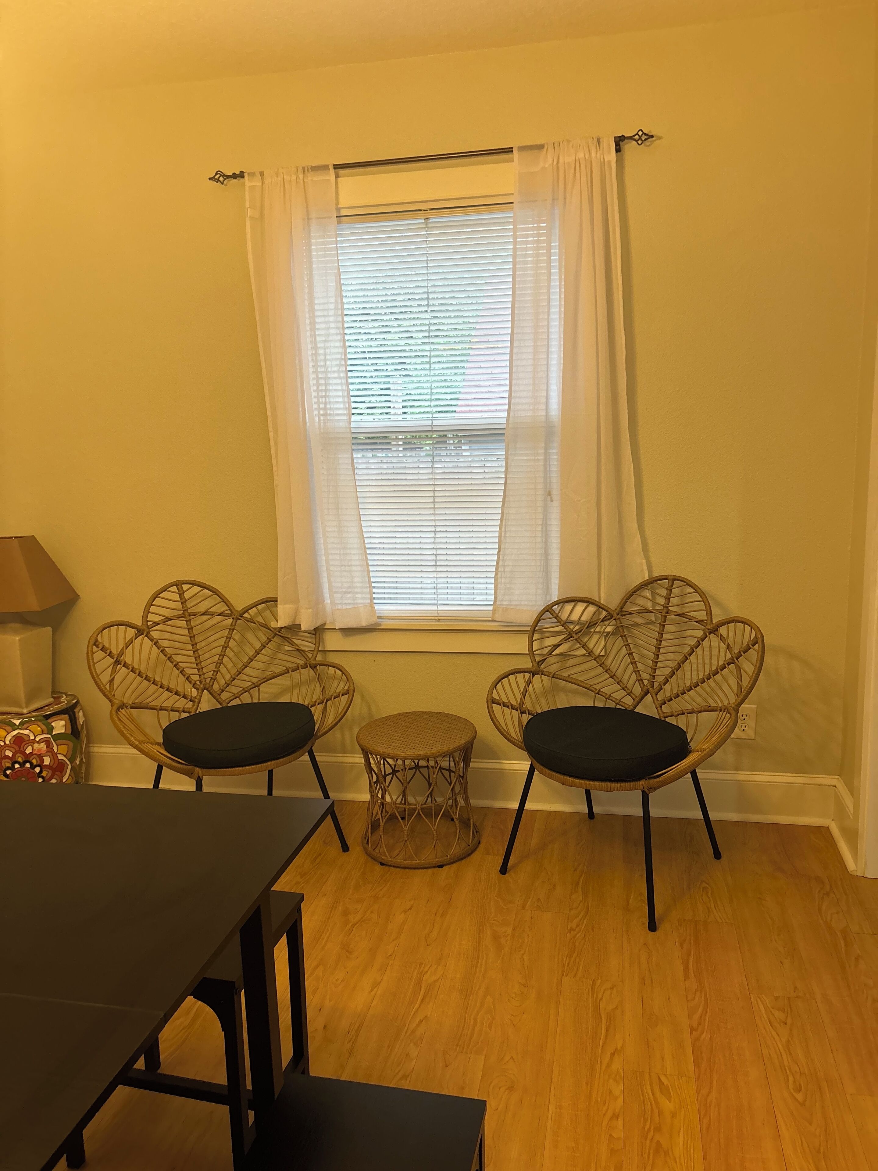 A room with two wicker chairs, a small round table, and a window with white curtains.