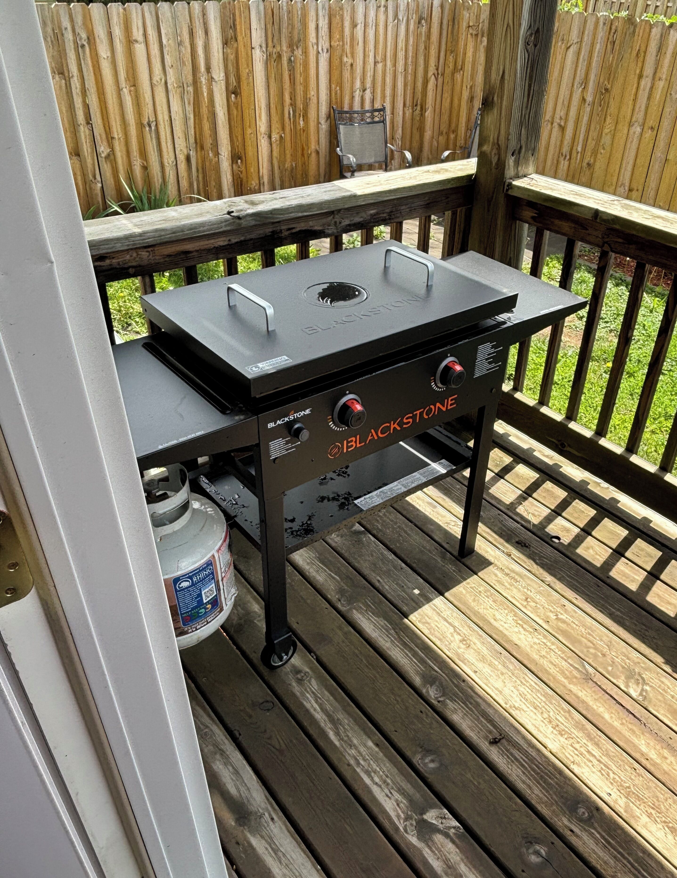 Una parrilla Blackstone sobre una terraza de madera, con una cerca de madera al fondo.