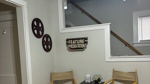 Una habitación con un cartel de presentación especial, dos sillas de director, una mesita con una caja de pañuelos y un ventilador de techo.