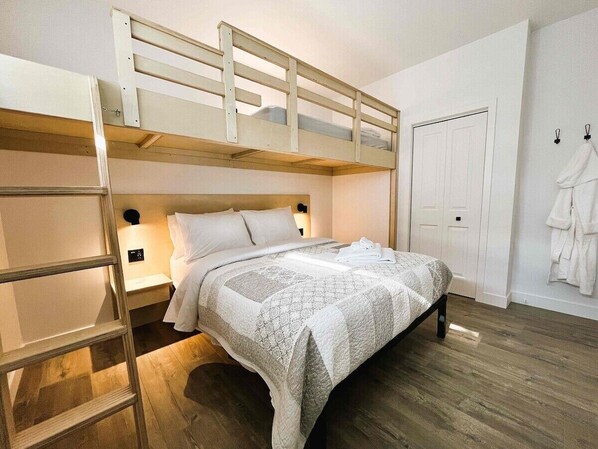 A bunk bed room with a ladder, a bedside table, and a white door.