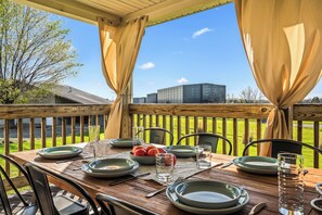 Une terrasse en bois avec une table dressée pour le repas, comprenant des assiettes, des verres et un saladier rempli de fruits.