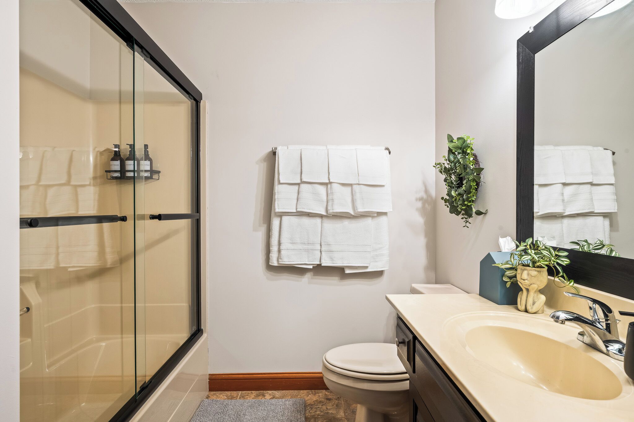 Un bagno con cabina doccia in vetro, un water, un lavandino con specchio e due asciugamani appesi al muro.