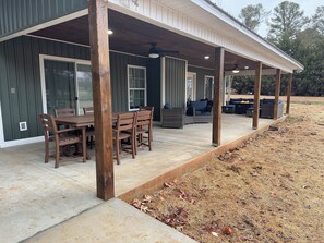 A covered patio area with a dining table and chairs, a seating area with sofas and cushions, and a wooden deck.