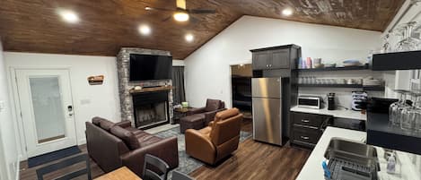 Una cocina moderna con refrigerador integrado, un comedor con mesa y sillas de madera, y una sala de estar con sofás de cuero y chimenea de piedra.