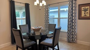A dining area with a glass table, four chairs, a chandelier, and patterned curtains. - Charming 3-bedroom house with AC, WiFi in lovely Alachua (Alachua)