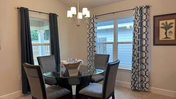 A dining area with a glass table, four chairs, a chandelier, and patterned curtains.