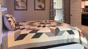 A bedroom with a bed, two wall art pieces, a window with a geometric curtain, and a door leading to a kitchen. - Charming 3-bedroom house with AC, WiFi in lovely Alachua (Alachua)