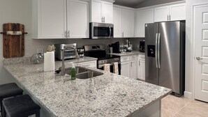A modern kitchen with white cabinets, stainless steel appliances, granite countertops, and a built-in oven. - Charming 3-bedroom house with AC, WiFi in lovely Alachua (Alachua)