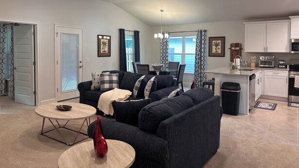A modern living room with a dark grey sectional sofa, a round coffee table, and a red vase. A dining area with a table and chairs is visible in the background. - Charming 3-bedroom house with AC, WiFi in lovely Alachua (Alachua)