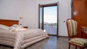 Une chambre d’hôtel avec un lit, une chaise, une table recouverte d’une nappe blanche et un balcon avec vue.
