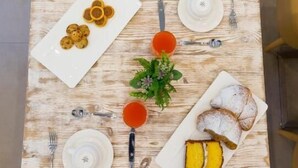 Une table carrée, dotée d’un plateau en bois rustique, mise avec des assiettes, des couverts et une petite plante en pot.