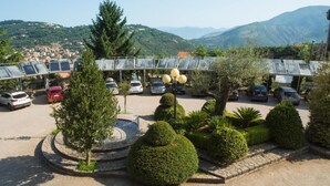 Un espace de stationnement équipé de panneaux solaires, agrémenté d’arbustes soigneusement taillés, et offrant une vue sur une ville et des montagnes en arrière-plan.