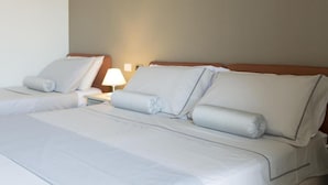 Une chambre d’hôtel avec deux lits, une table de chevet avec une lampe et un mur sobre.