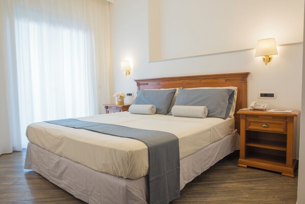 Habitación de hotel con una cama grande, dos mesitas de noche, una lámpara y un ventanal con cortinas.