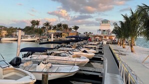 Un puerto deportivo con varias embarcaciones amarradas, un faro y una playa con palmeras.