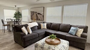 Una sala de estar con un sofá modular, una mesa de centro con una planta, y un comedor con una mesa y sillas.