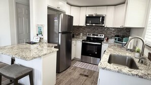 Una cocina moderna con armarios blancos, un refrigerador de acero inoxidable, horno empotrado y microondas.