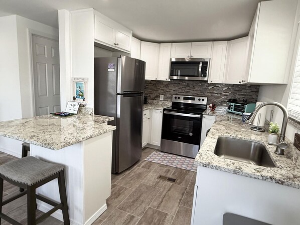 A modern kitchen with white cabinets, a stainless steel refrigerator, a built-in oven, and a microwave.