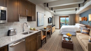 Una habitación de hotel moderna con cocina, comedor y una cama grande con vista al balcón.