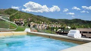Zona de piscina con vistas a un pueblo en la ladera, incluyendo edificios y un telesilla.