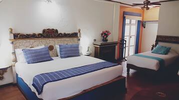 Une chambre d’hôtel avec deux lits, une petite table ornée d’un vase de fleurs, un ventilateur de plafond et une vue sur l’extérieur.