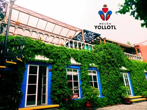 A building with blue doors and windows, covered in green ivy, and a balcony with white balustrades. - Meson Yollotl (Puebla)