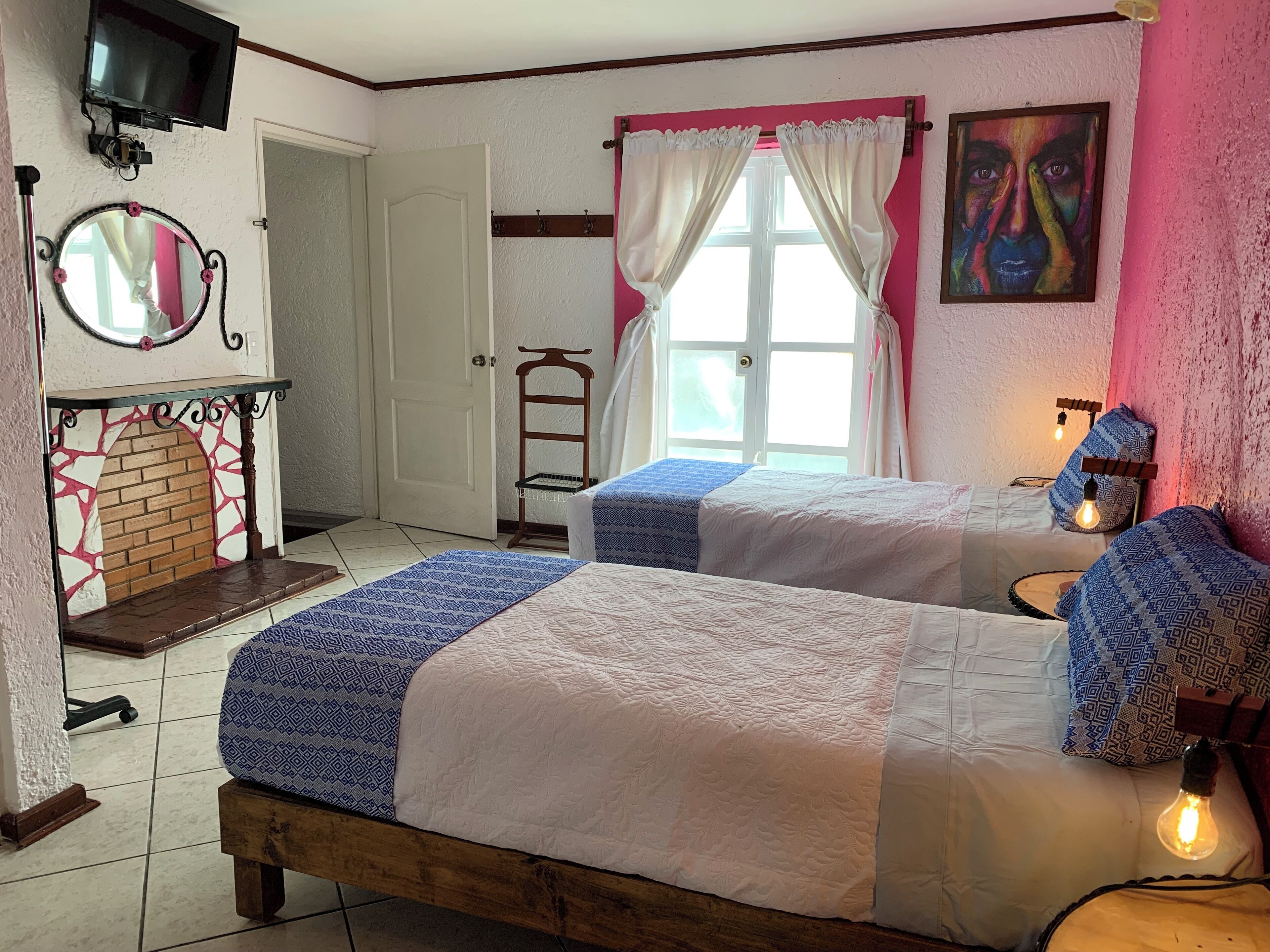 A room with two beds, a fireplace, a TV, and a window with curtains.