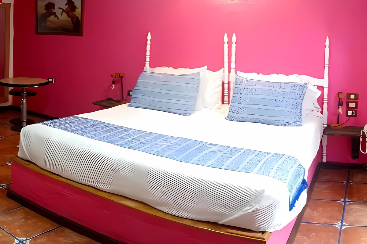 A bedroom with a bed, a nightstand, a chair, and a painting on the wall.
